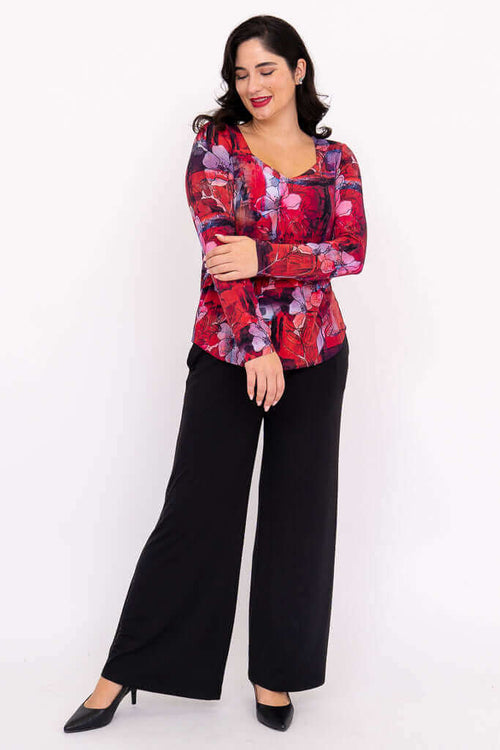 Full-body view of woman in a red floral long sleeve top and black pants