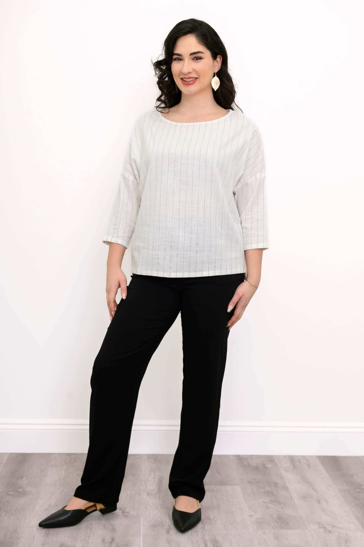 Full view of woman in light striped top and black pants, styled with pointed flats