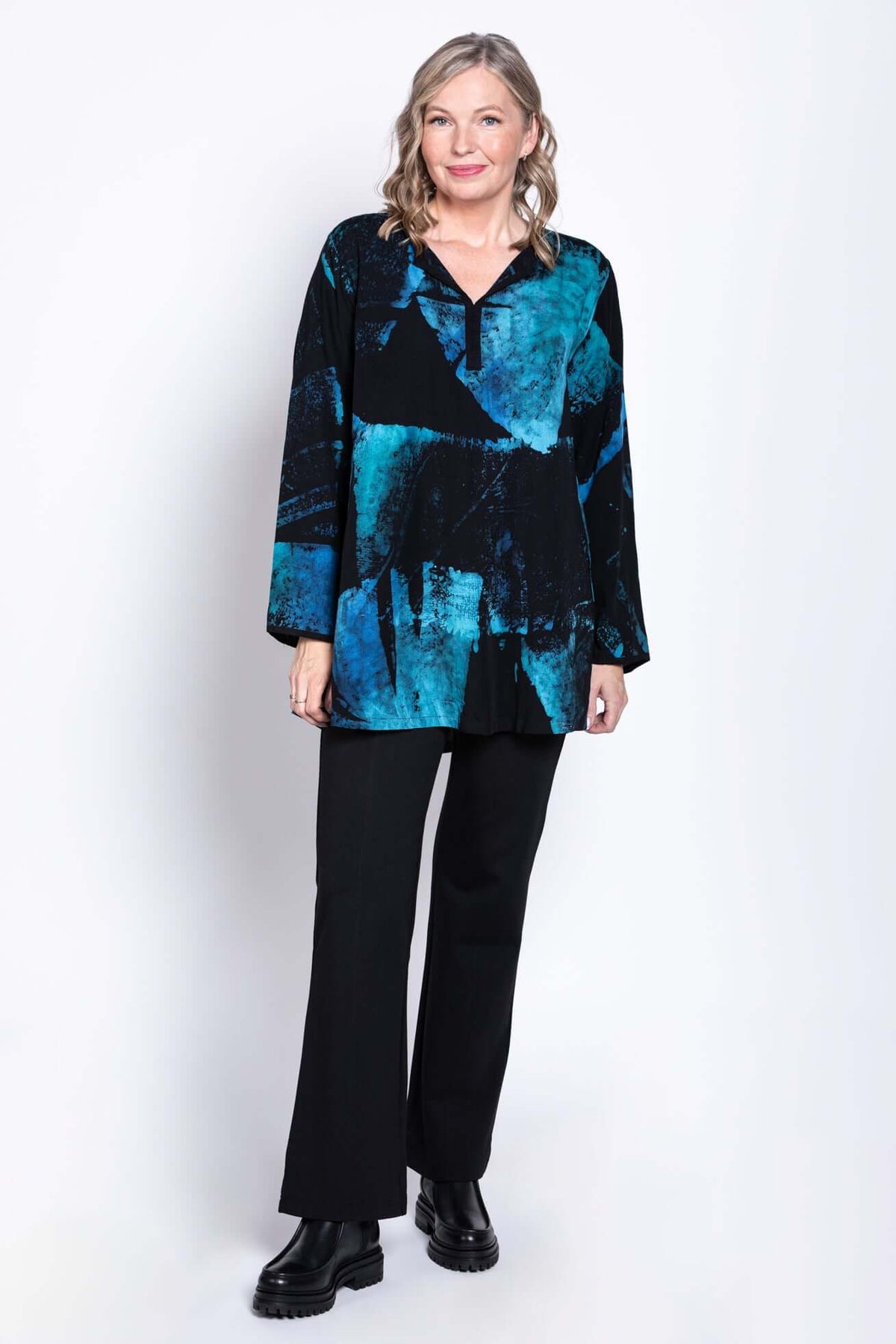 Full body view of a woman in a black and blue Batik blouse paired with black pants and boots