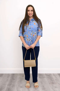Full body view of a woman in a blue floral blouse with dark pants and beige accessories