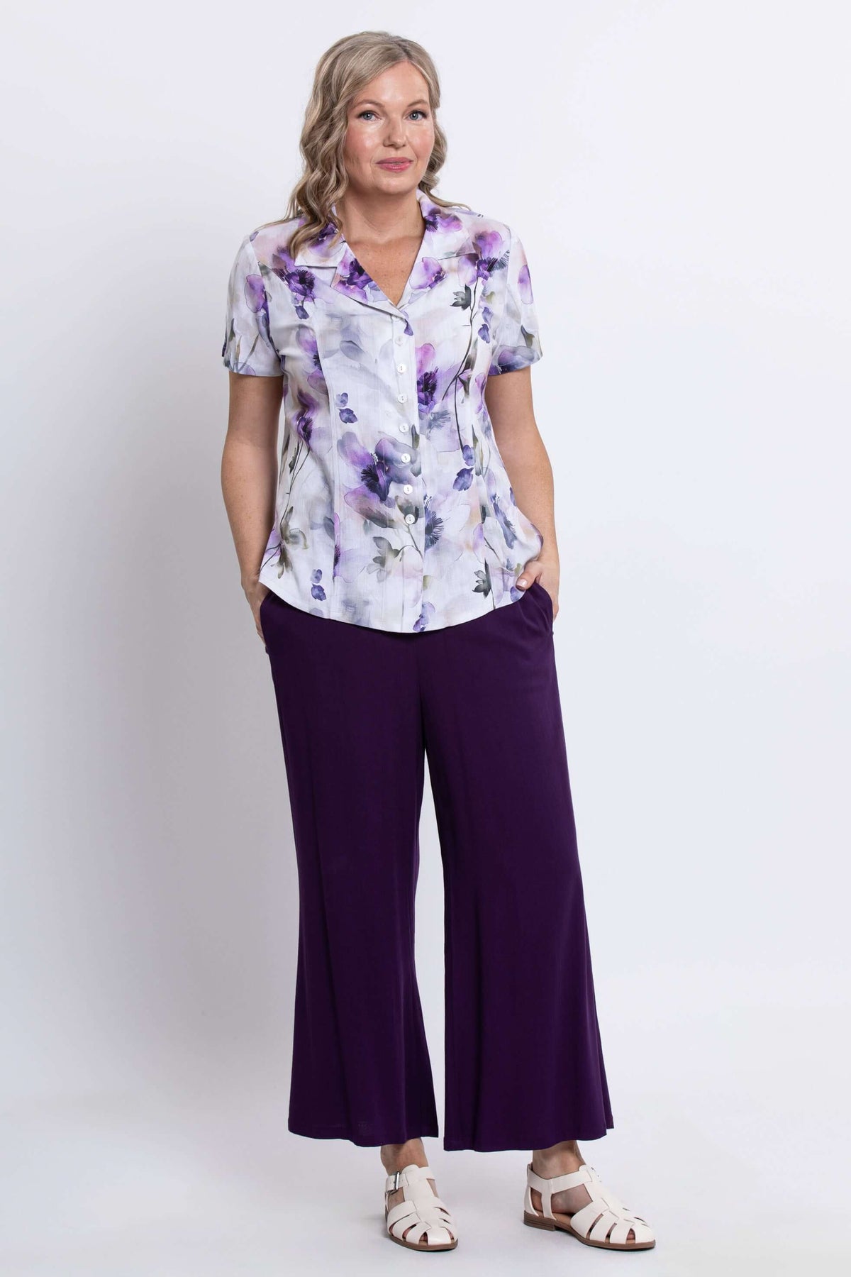 Woman wearing a purple floral print button-up shirt and wide-leg purple pants, front view