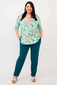 Full-length view of woman in blue floral V-neck top and teal pants