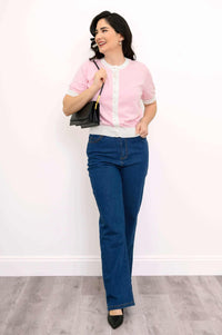 Full body view of woman in retro pink sweater and jeans with a black handbag