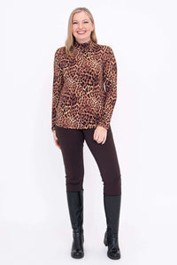 Full view of a woman in a leopard print mock neck top, dark pants, and boots