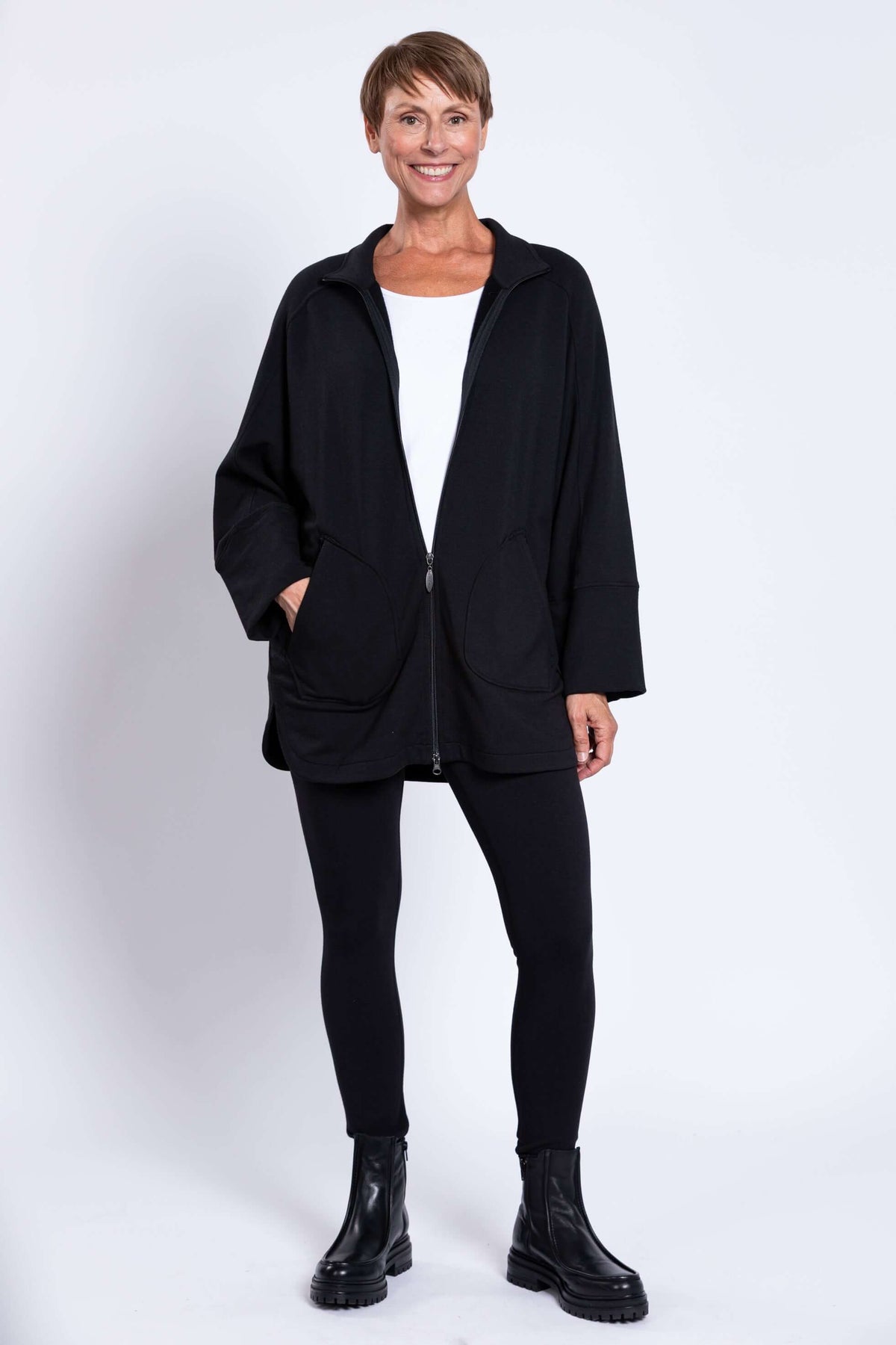 Woman in full view wearing black zip-up jacket, black leggings, and boots
