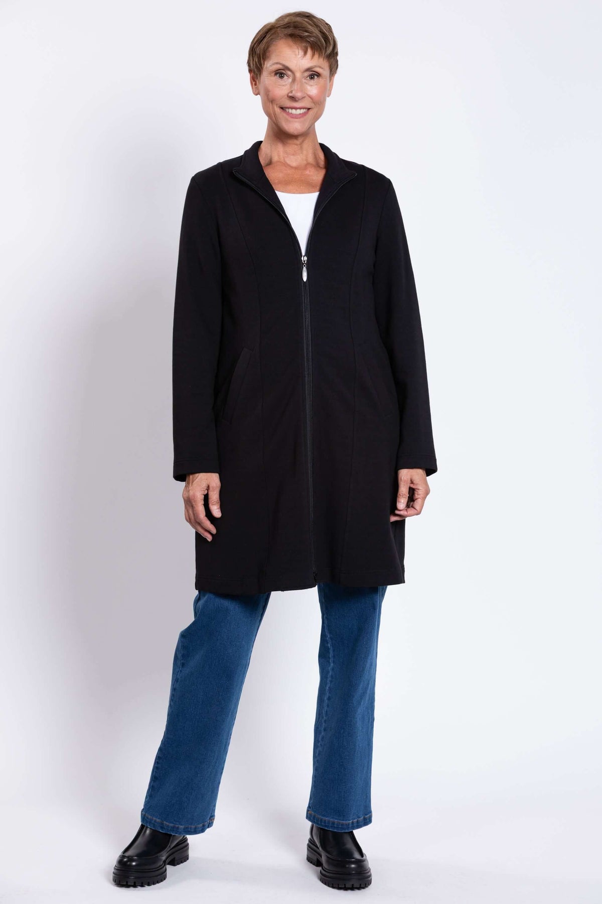 Full view of woman in a black knee-length coat with zipper and blue jeans