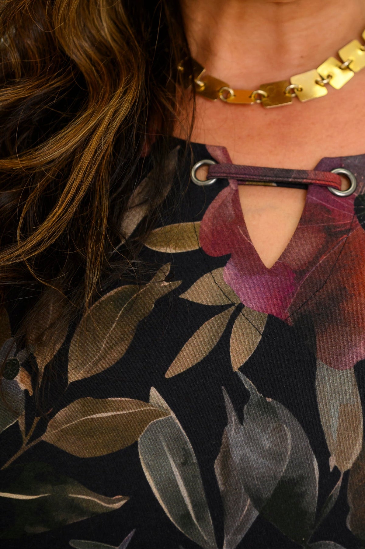 Close-up of a women's colorful floral knit top, highlighting the notched keyhole neckline and gold necklace.