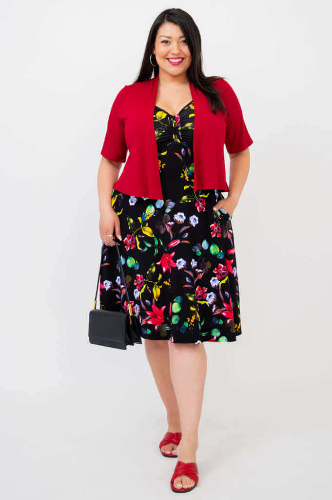 Woman styling black floral fit and flare dress with red cropped cardigan and black handbag