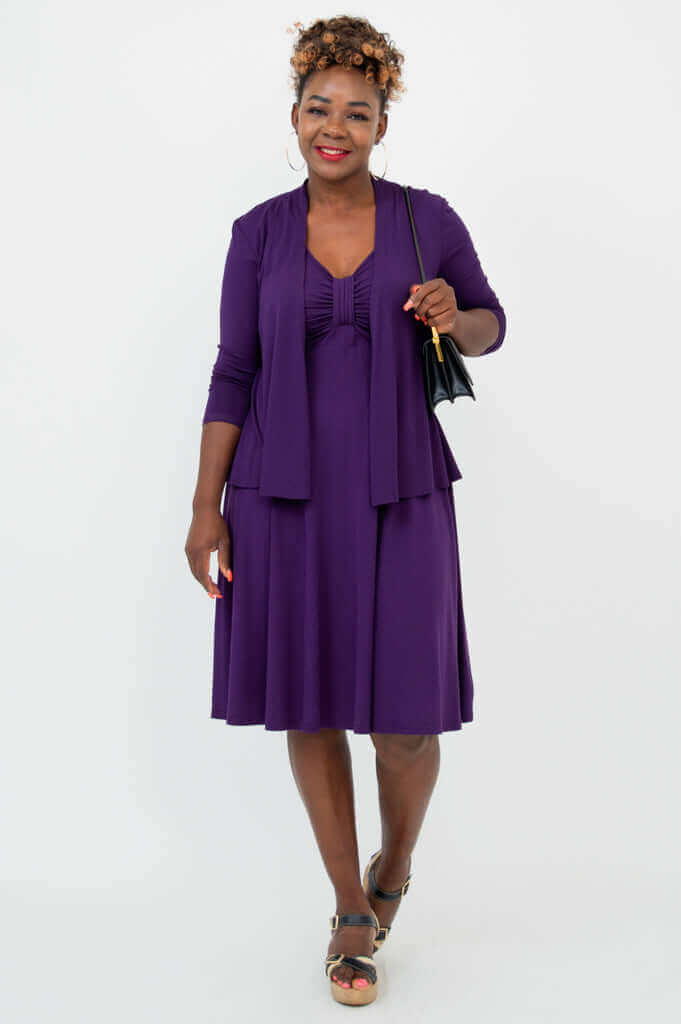 Woman wearing violet dress and matching cardigan, holding a black purse