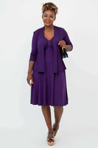 Woman wearing violet dress and matching cardigan, holding a black purse