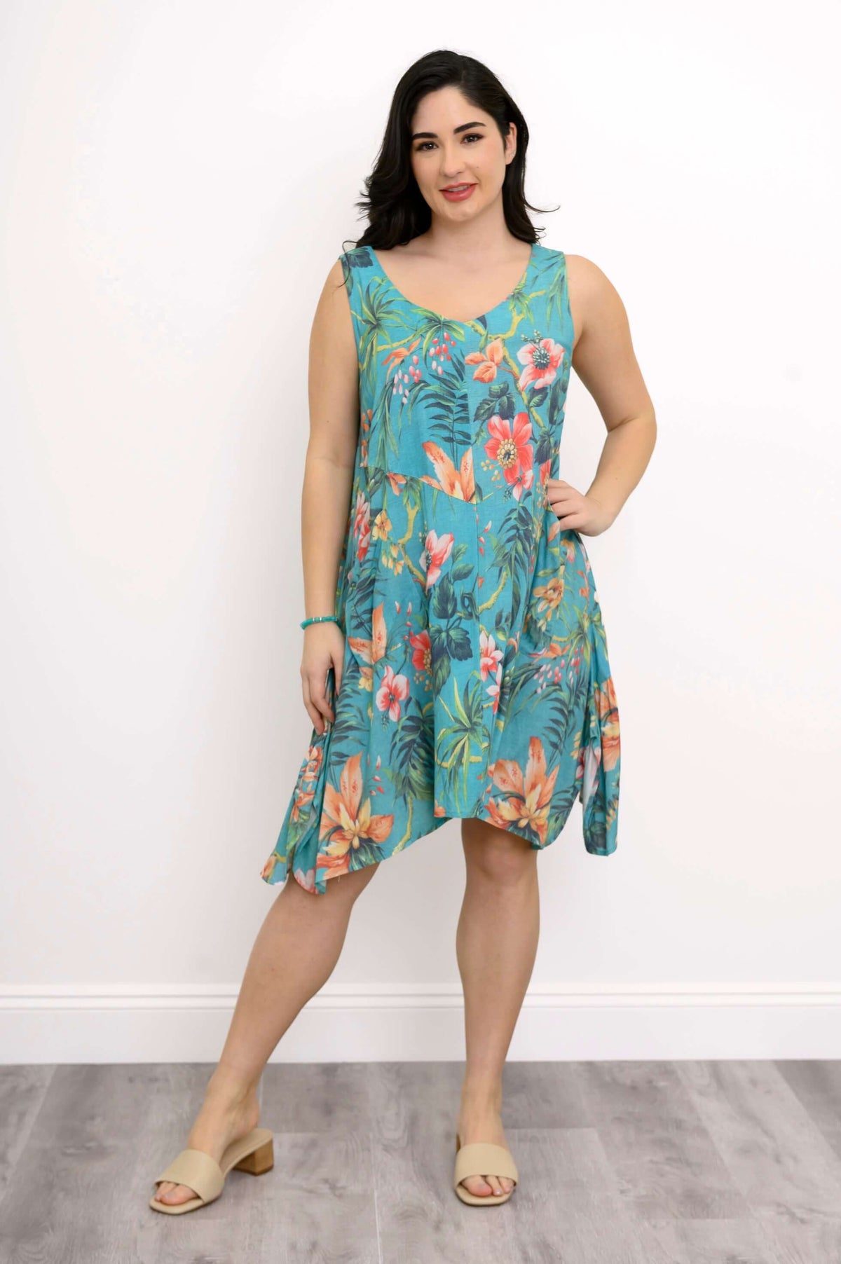 Woman modeling turquoise sleeveless dress with tropical floral print, hand on hip