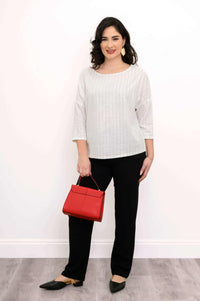 Woman holding a red handbag, wearing a white pinstripe top and black pants