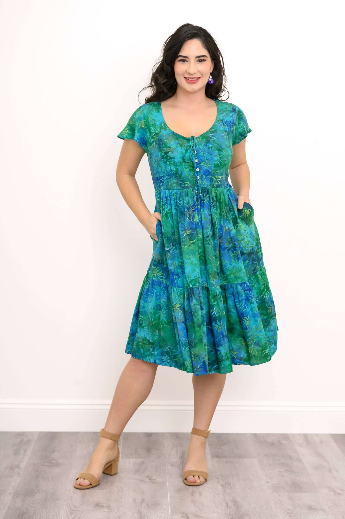 Woman in a green and blue dress with hands in the side pockets, showcasing flutter sleeves