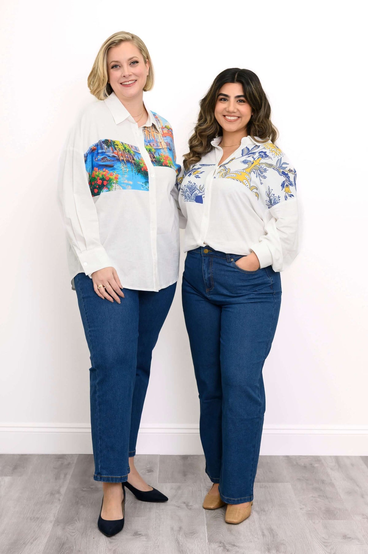 Two women wearing printed white blouses and blue jeans, one with Venice print