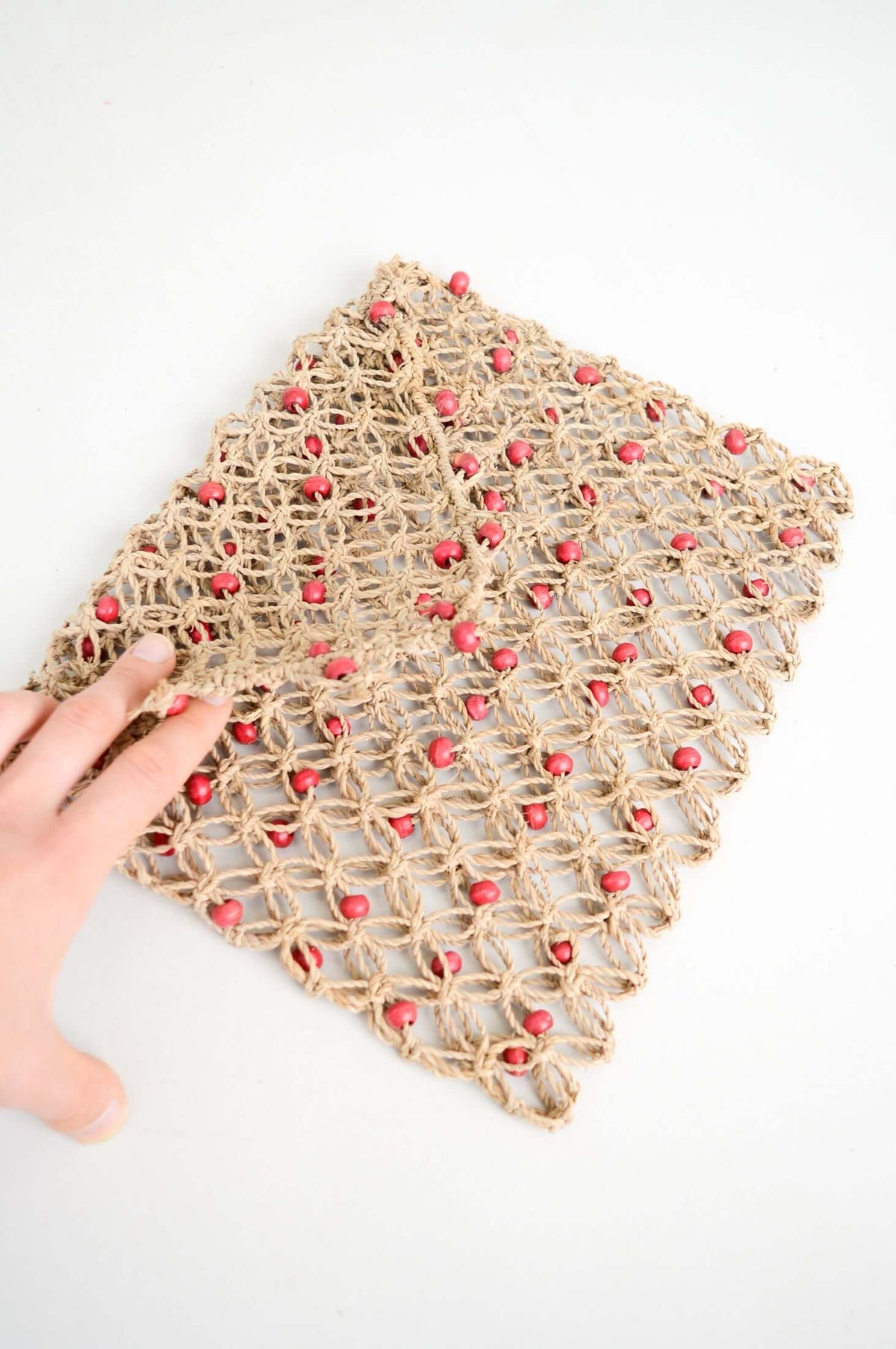 Hand holding flap of handwoven rattan purse with coral bead details
