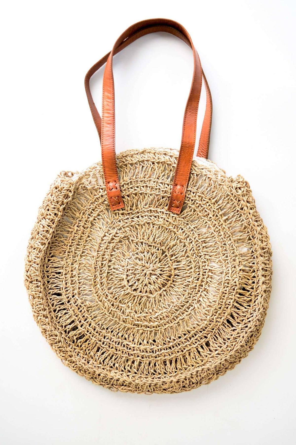 Round hand woven rattan bag with brown leather handles on a white background