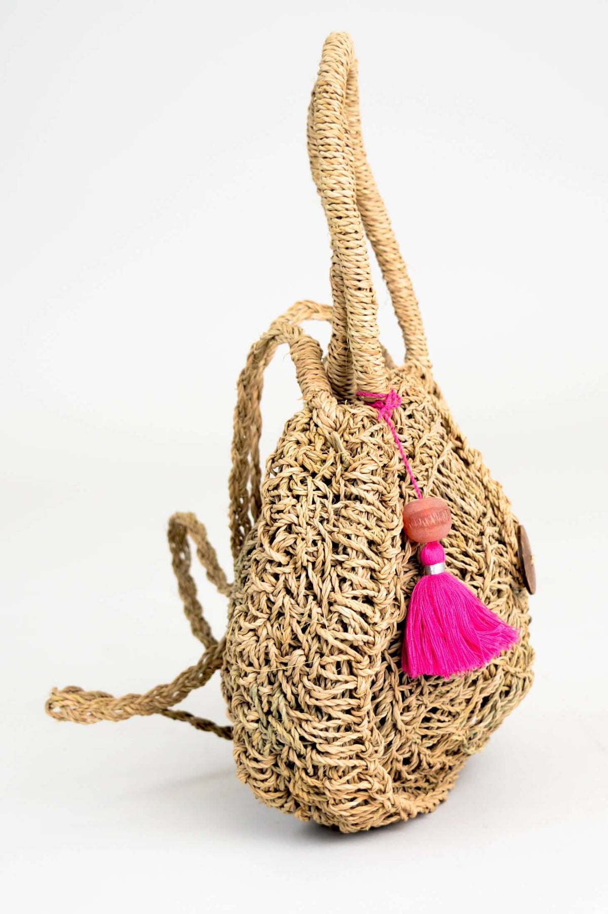 Side profile of a hand woven rattan bag showing pink pom-pom and textured design