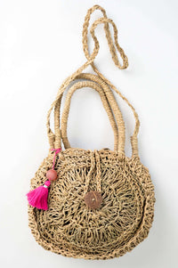 Top-down view of hand woven rattan bag with pink pom-pom and long strap