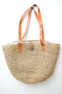 Hand woven rattan bag with tan leather handles against a white background