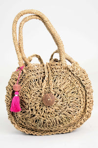 Front view of a hand woven rattan circle bag with pink pom-pom detail