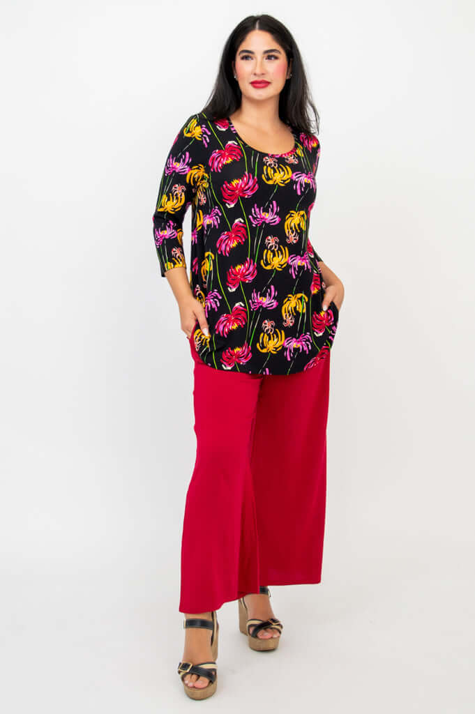 Model posing with hands in pockets, dressed in black floral bamboo top and red pants