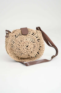 Handwoven round rattan bag with brown leather handle and strap, front view