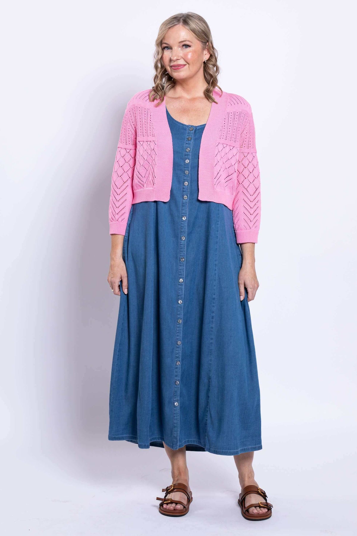 Model facing forward in pink cropped cardigan paired with blue dress and brown sandals