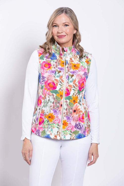 Woman wearing a vibrant floral print vest with a white long-sleeve top and white pants