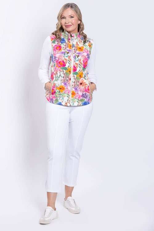 Full view of a woman in a floral print vest, hands in pockets, paired with white outfit and sneakers