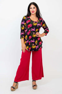 Model standing with hand on hip, showcasing black top with chrysanthemum blooms and red pants