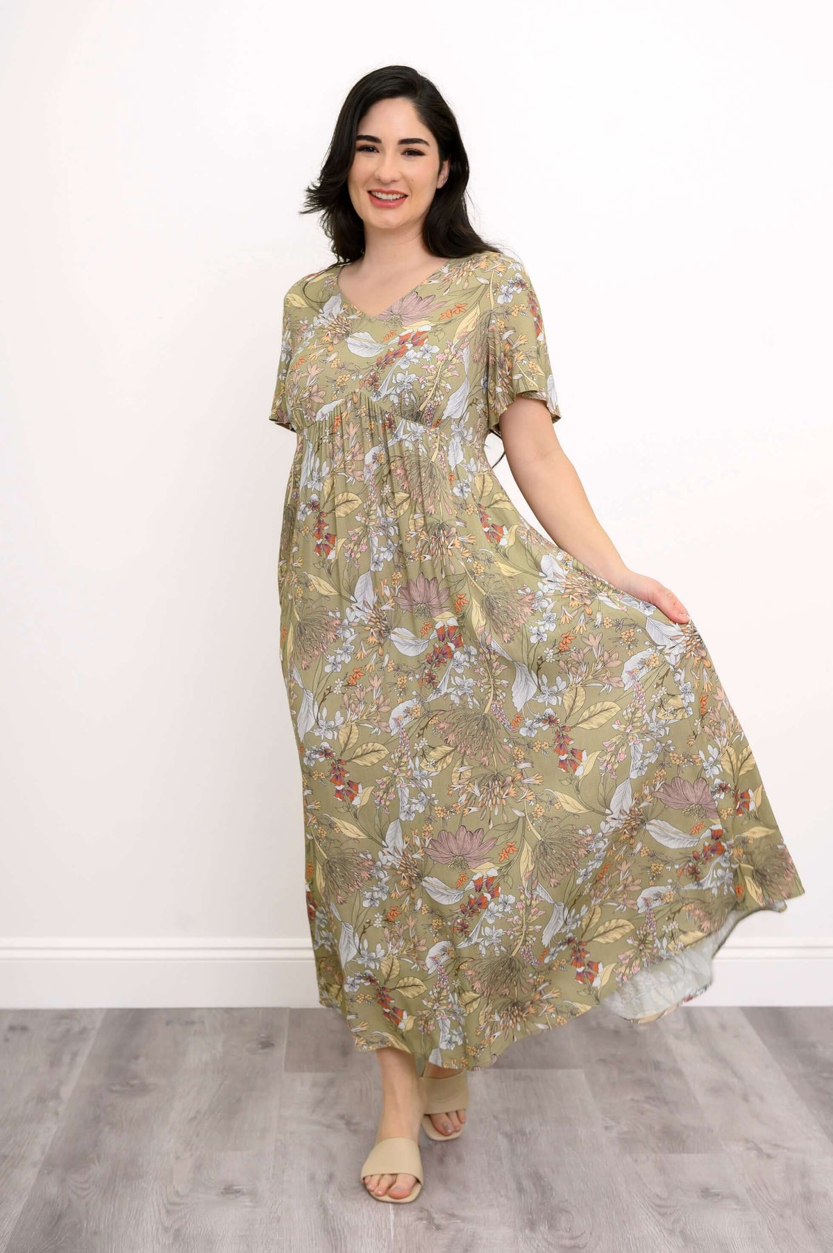 Woman holding the skirt of a green floral maxi dress with short flutter sleeves