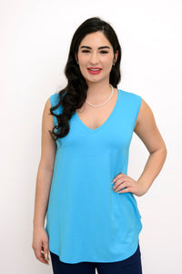 Woman wearing a bright blue sleeveless top and navy pants against a white background, front view