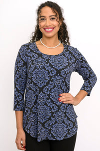 Front view of a smiling woman wearing a blue patterned rounded hem top with 3/4 sleeves and a scoop neckline.