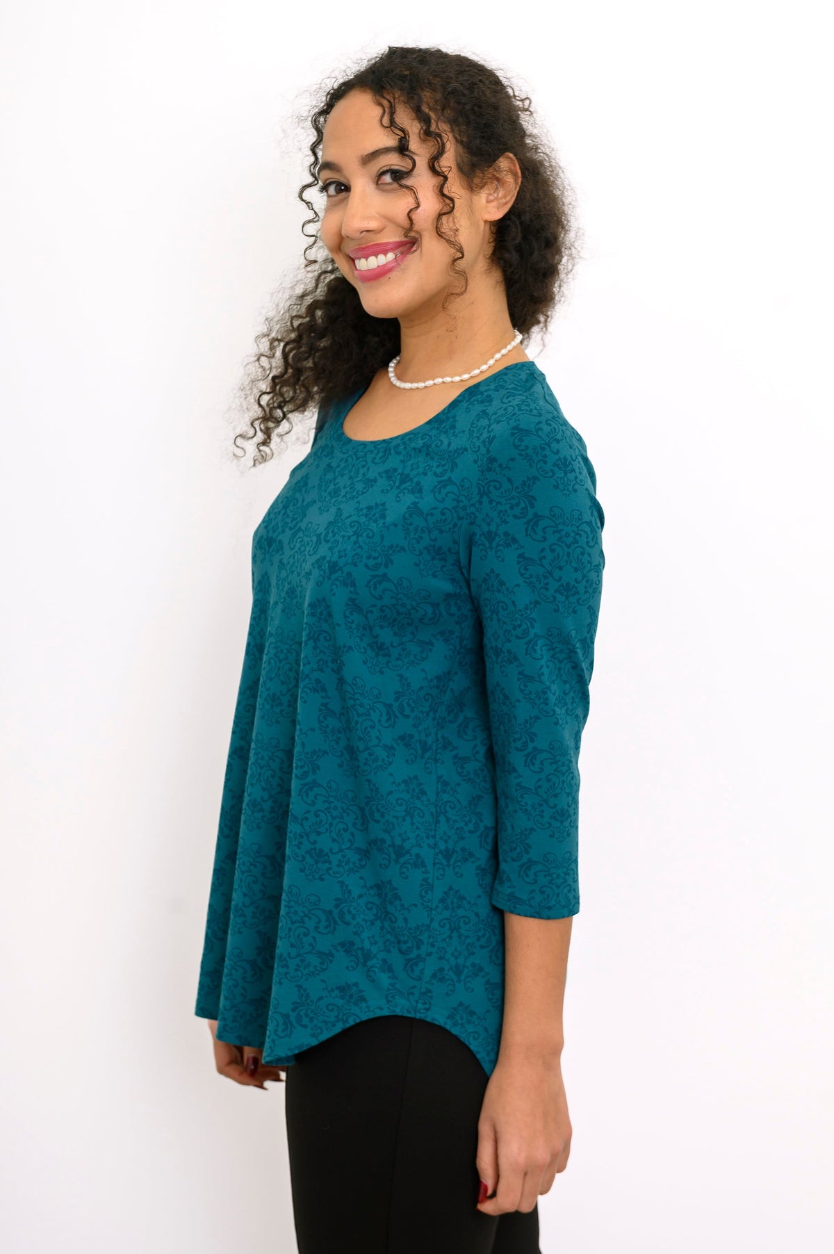 Profile shot of a women's teal geometric print 3/4 sleeve blouse, styled with casual black trousers.