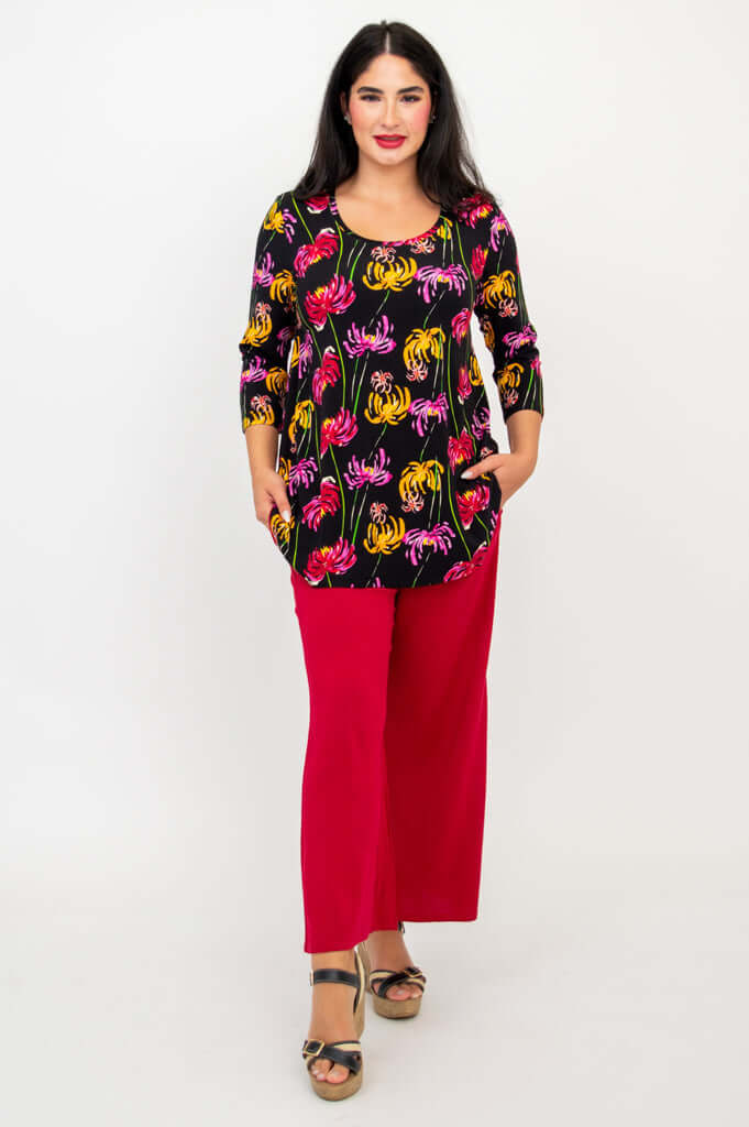 Model standing with one hand in pocket, wearing black chrysanthemum print top and red pants