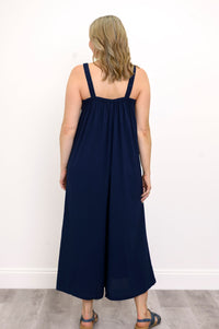 Back view, woman wearing a navy blue jumpsuit and sandals against a white background