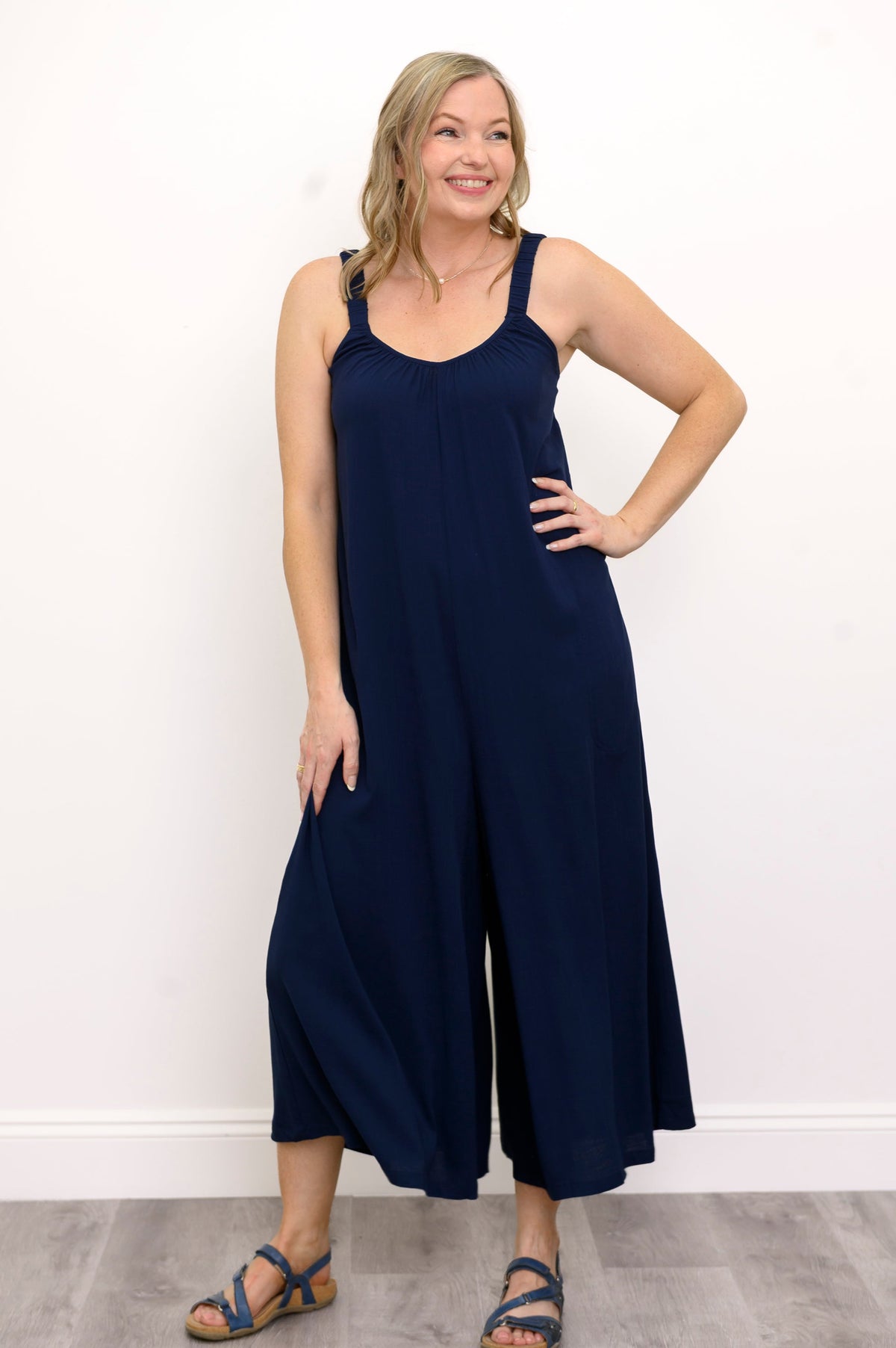 Front view, woman wearing a navy blue jumpsuit, and sandals against a white background