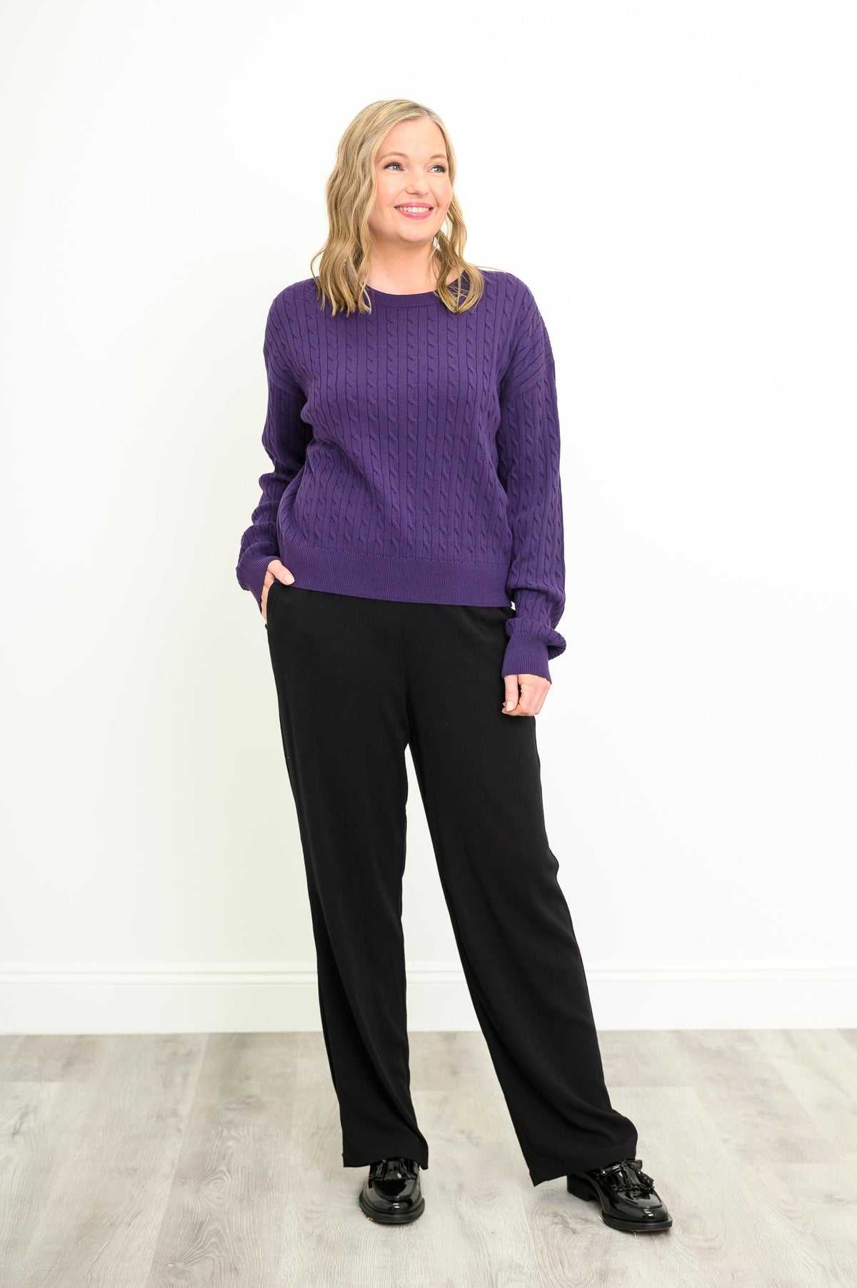 Classic plum-colored knit top featuring patterned cable textures and ribbed cuffs, styled with dark trousers.