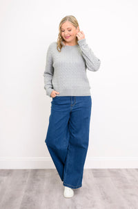 Angled view of a silver-toned long-sleeve textured sweater on a model, standing against a plain white wall.