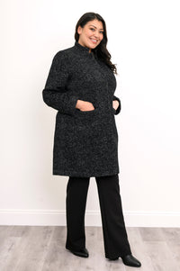 Woman wearing black/dark grey collared coat with hands in pockets and a black pants