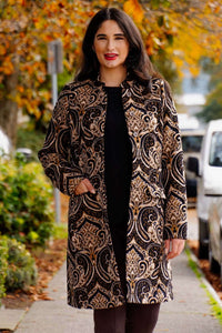 Woman wearing the Julia Coat with gold and black jacquard pattern, autumn background