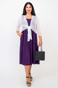 Front view of woman in plum dress with white shrug and black handbag