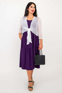 Woman in plum dress and white shrug holding black handbag