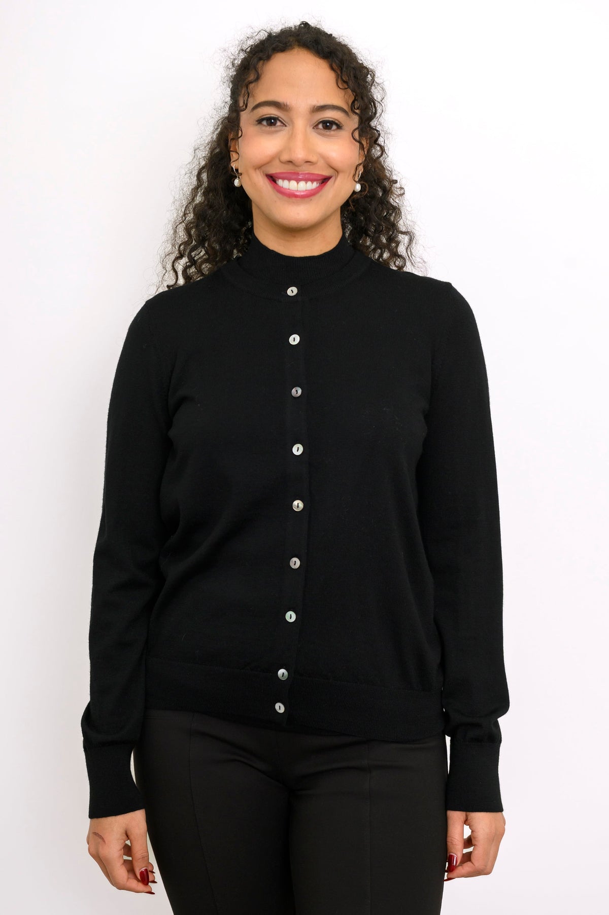 Close up front view of a smiling woman wearing a black fine knit merino wool crewneck cardigan.