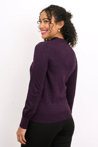 Back view of woman wearing a purple cardigan on a purple top and black pants against a background