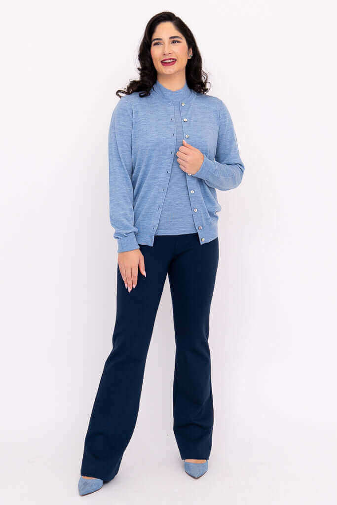 Woman in blue Merino cardigan and navy pants, front facing with hand on chest