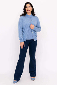 Woman in blue Merino cardigan and navy pants, front facing with hand on chest