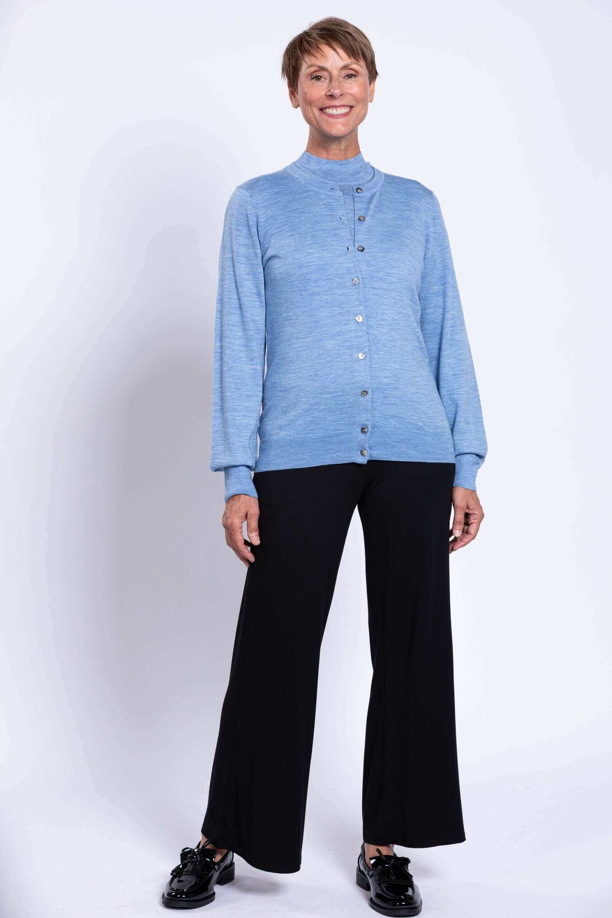 Woman standing, wearing blue cardigan and black pants, hands at side