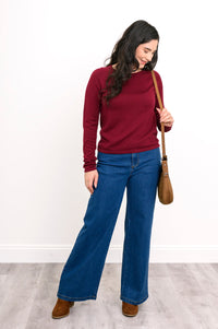 Model wearing a rich wine-red sweater layer and blue denim pants, styled for a comfortable, casual winter look.