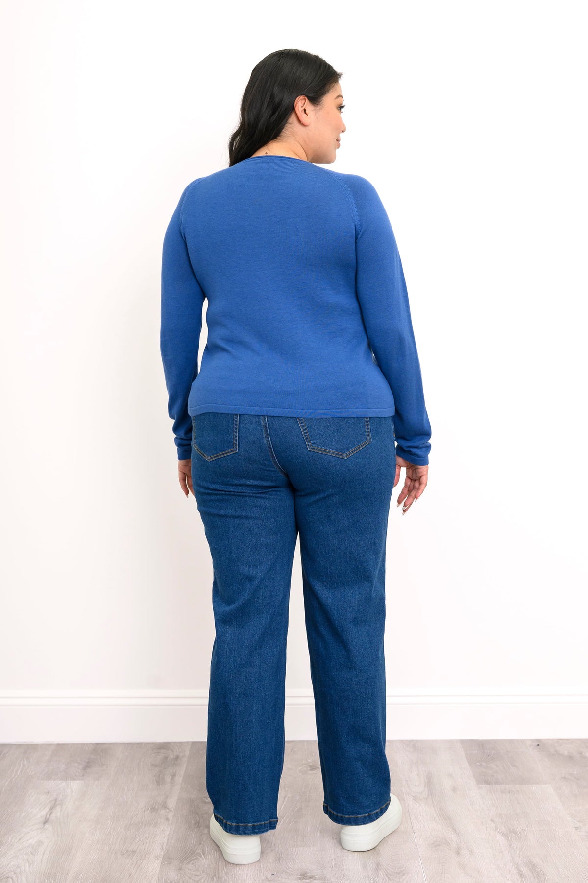 Back view of a pacific blue raglan sweater, showcasing a seamless rear panel, long sleeves, and dark denim jeans.